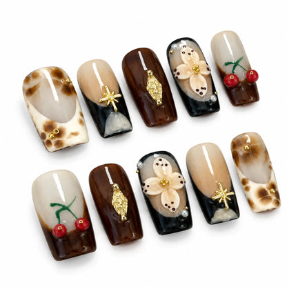 Angled view of brown and nude Long Square nails with 3D flowers red cherries gold charms and pearls
