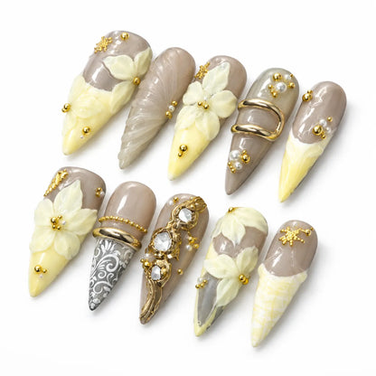 Angled view of taupe nude and butter-yellow Long Stiletto nails with pearls and sculpted florals