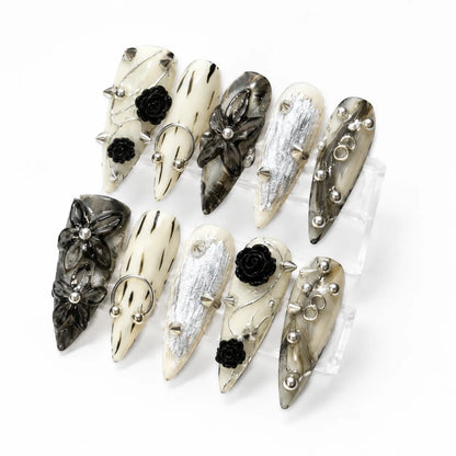 Angled view of Inkthorn Noir punk nails showing raised black roses, metal rings, studs, and silver foil
