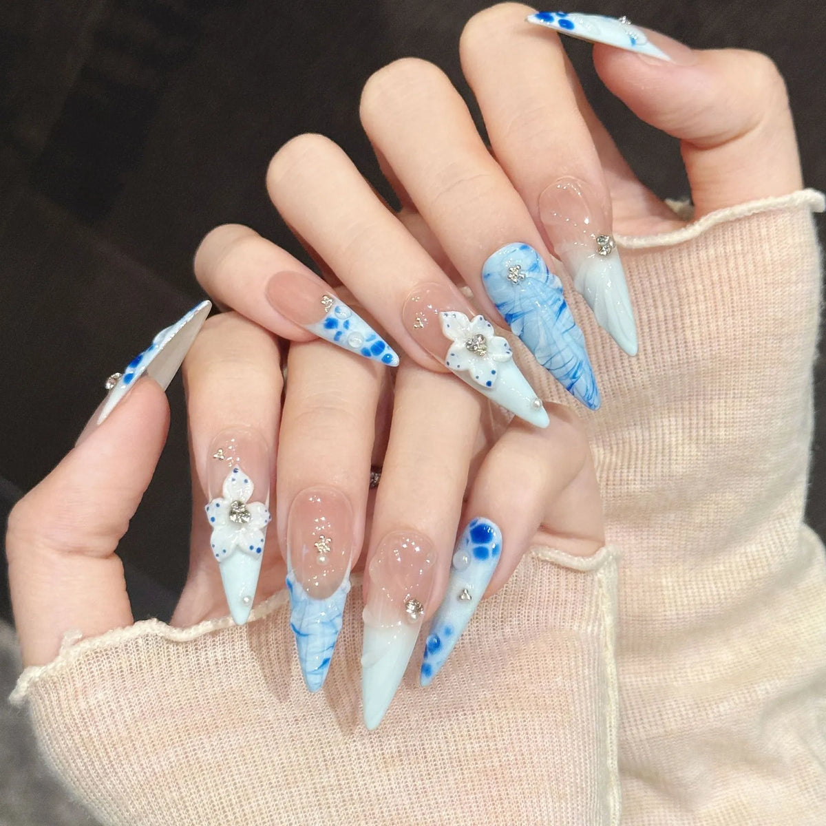 Porcelain Tide stiletto nails angled view showing powder blue gradient, water ripples, and 3D ceramic flowers