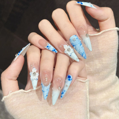 Porcelain Tide stiletto nails angled view showing powder blue gradient, water ripples, and 3D ceramic flowers