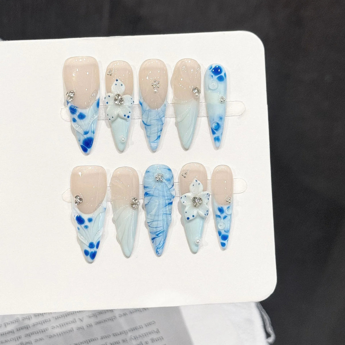 Porcelain Tide long stiletto press-on nails with blue gradient, water ripples, and 3D floral design on hand - lifestyle shot
