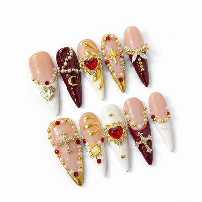 Angled view of blush ivory and wine-red Long Stiletto nails with crystal crosses heart gems and pearl chains